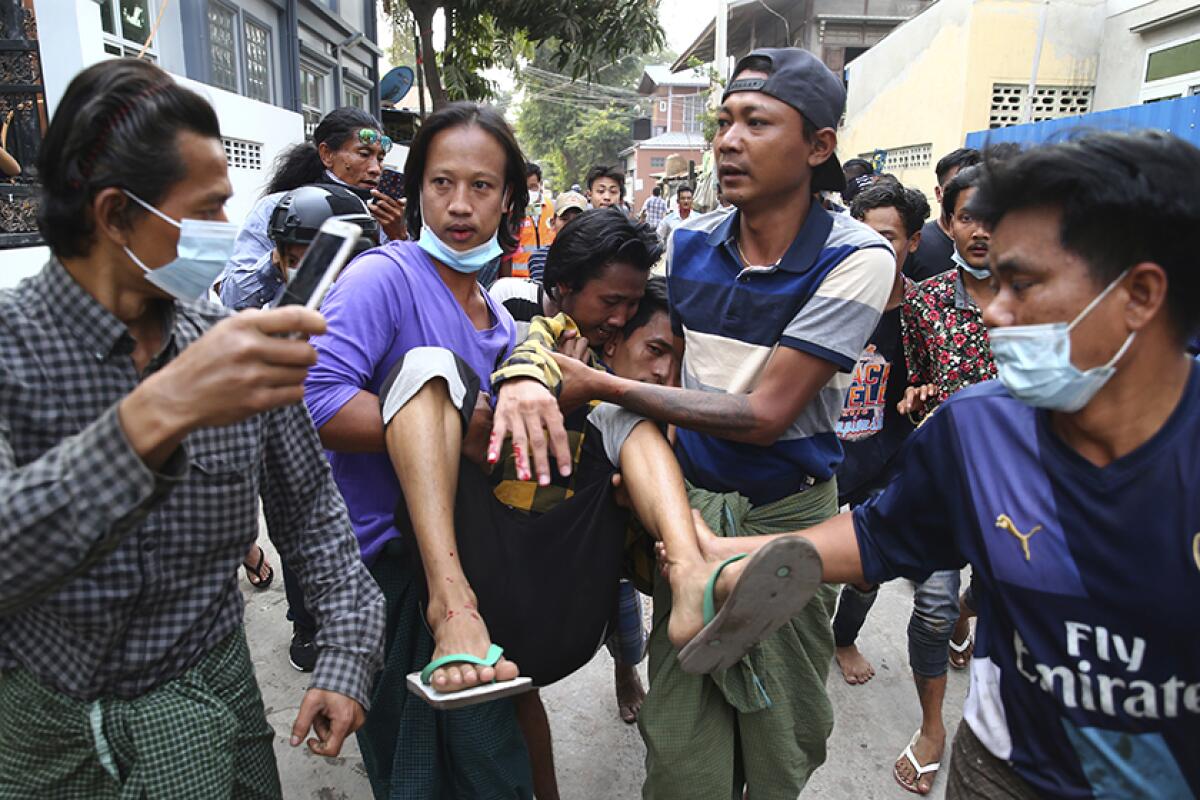 A man, left, holds his phone aloft as other people carry a man with blood on his fingers 