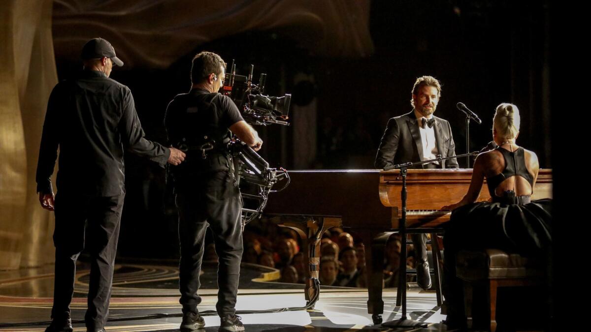 Shown from backstage, Cooper watches Gaga perform on the piano.