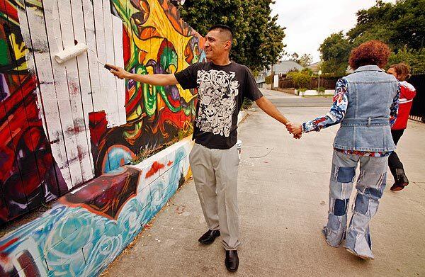 Valley Village resident Barbara Black holds Alexander Garcia's hand as he starts painting over a section of the 75-foot mural on a wall next to her home. Black had commissioned young artisits to paint the mural to add a splash of color to the drab alley. See full story