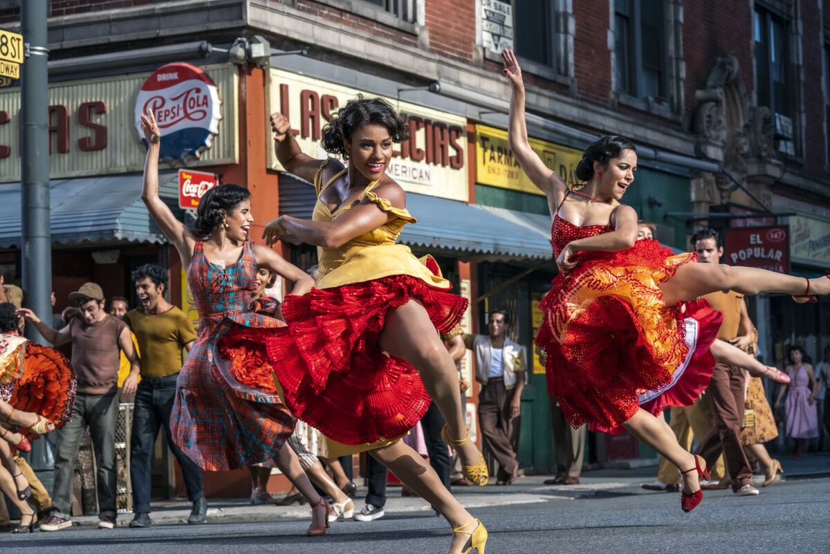 Women in colorful dresses dance on a New York street corner.
