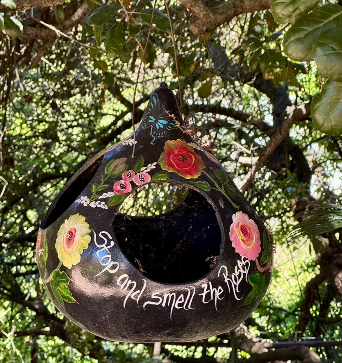 A hanging decorative gourd is painted with flowers and the words "Stop and smell the roses."