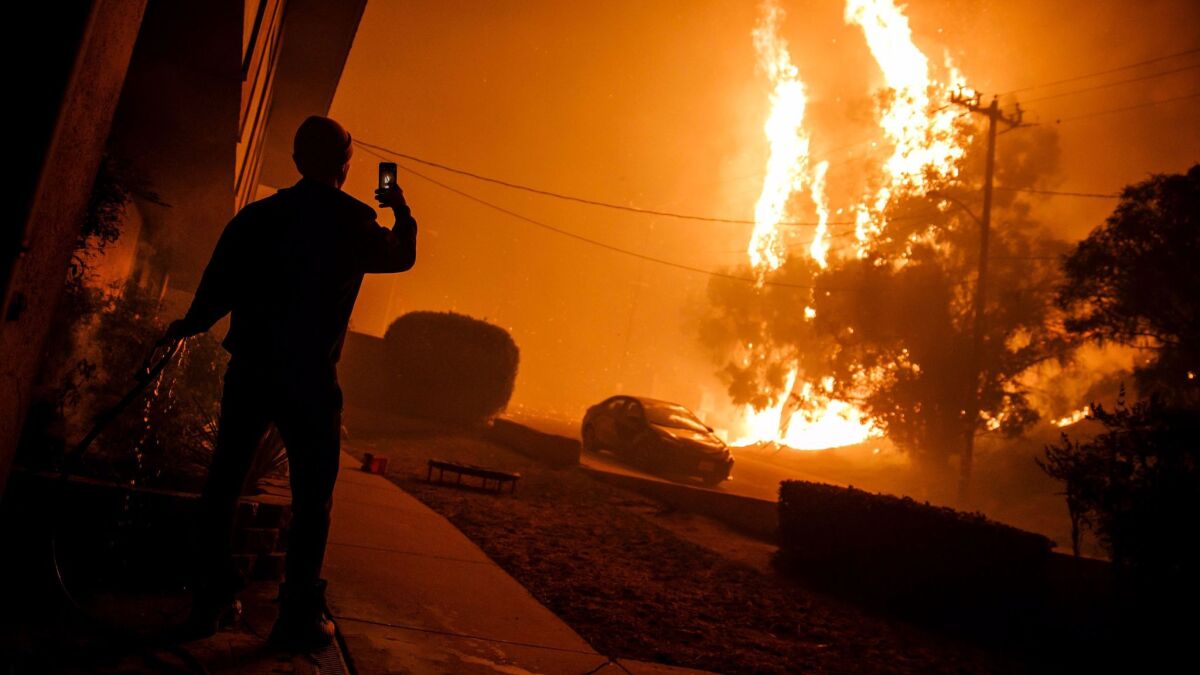 A man hoses down the front of a building and takes a picture of flames getting closer to homes in Ventura.