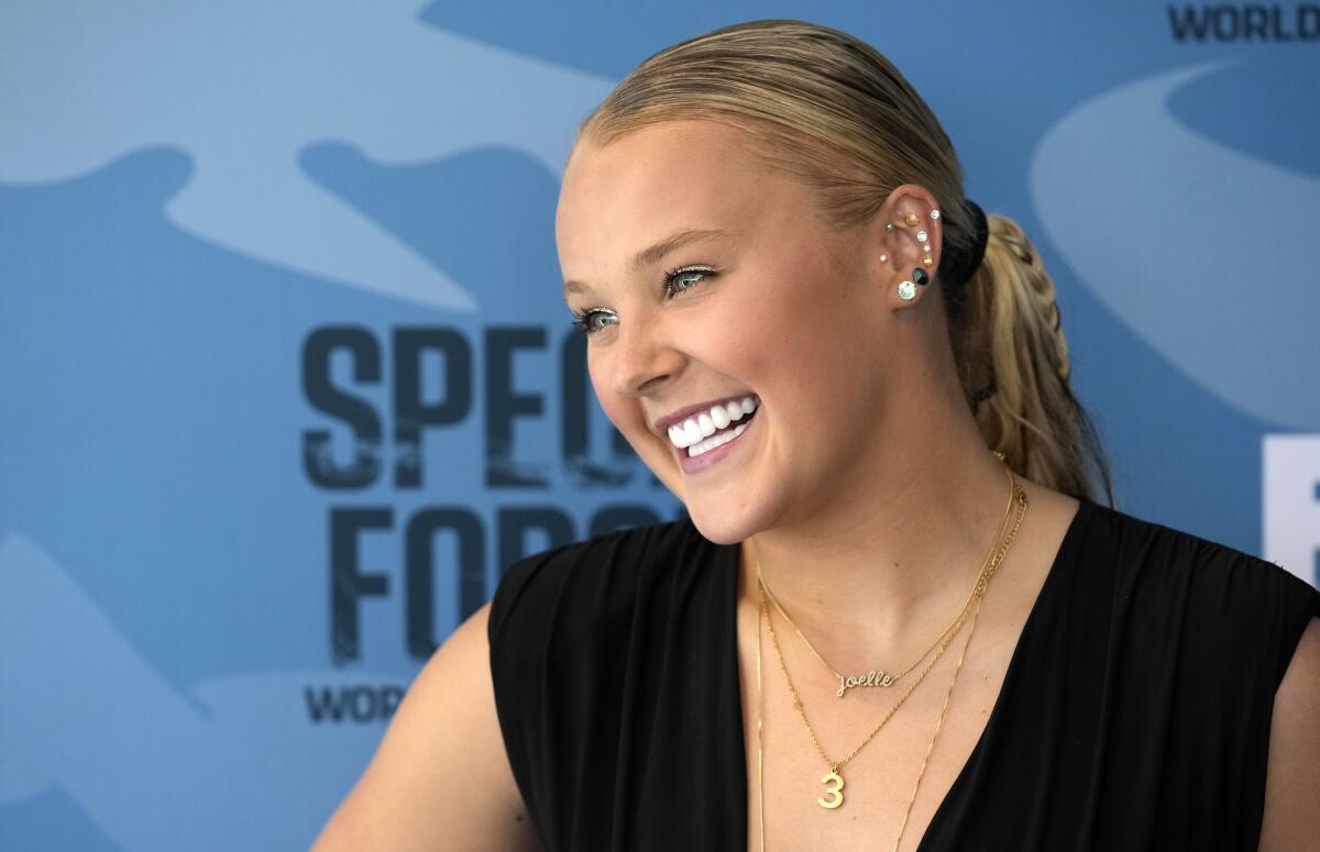 JoJo Siwa flashes a big smile off to the side while clad in a black sleeveless top