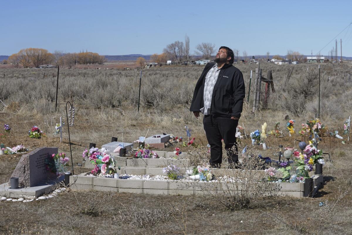 A  man stands next to a grave with a lot of flowers.