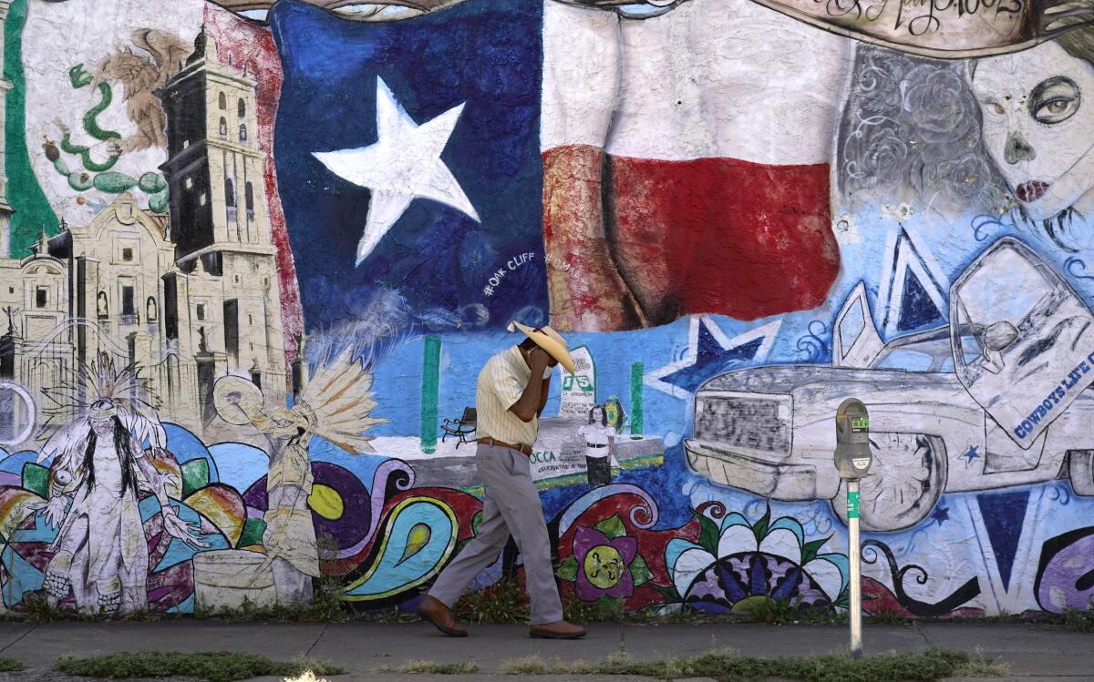 A man in a cowboy hat walks past a mural of Texas icons