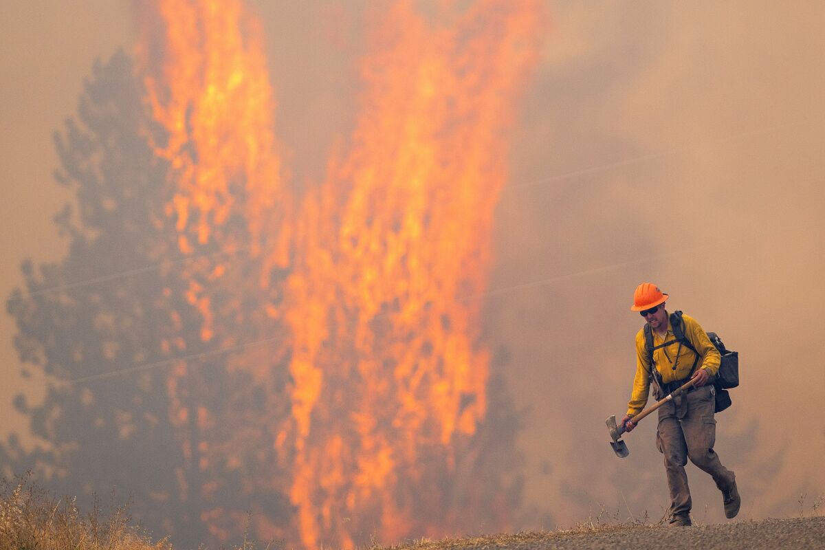 After walking down a gravel road to do recon on a fire cresting into the trees, a wildland firefighter grimaces as he walks back to his crew on Thursday, Aug. 12, 2021, at the Bedrock Fire north of Lenore, Idaho. Lenore is about 30 miles east of Lewiston, Idaho. (Pete Caster/Lewiston Tribune via AP)