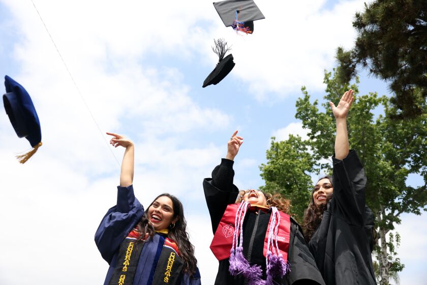 COVINA, CA - May 22: Cindy, Cecilia and Abigail Escobedo, left to right, throw their caps into the air while pose for a portrait wearing their graduation outfits at their home on the Sunday, May 22, 2022 in Covina, CA. The two sisters and mother are all attending higher education at the same time. Cecilia, the mother, decided to go back to school late in life and ultimately completed her master's and doctorate degrees alongside her eldest daughter, Cindy. Abigail, the younger daughter, also has attended college alongside her mother, and she is now a student at UC Santa Barbara. (Dania Maxwell / Los Angeles Times)