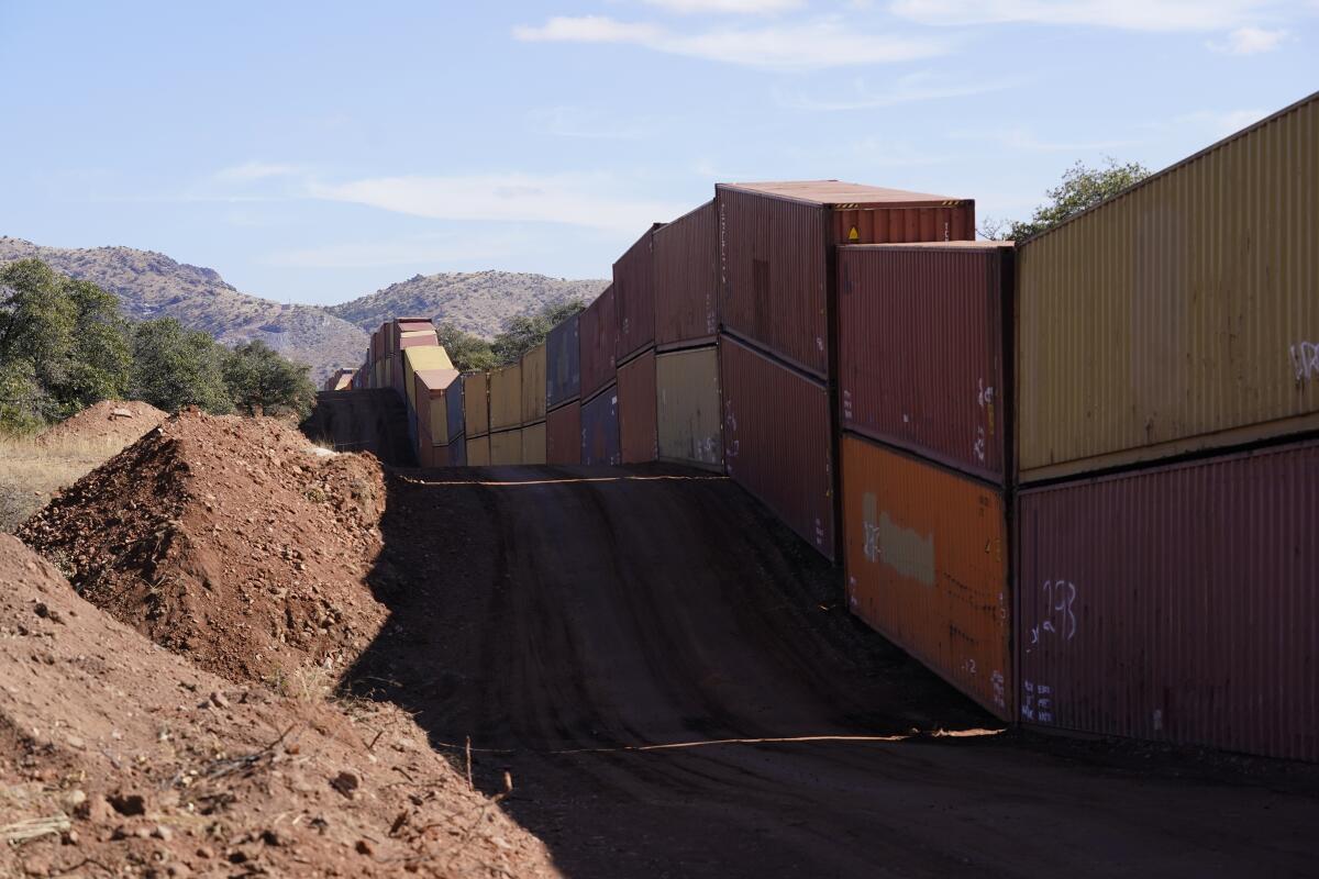 Double-stacked shipping containers line a rugged stretch of border in Arizona.