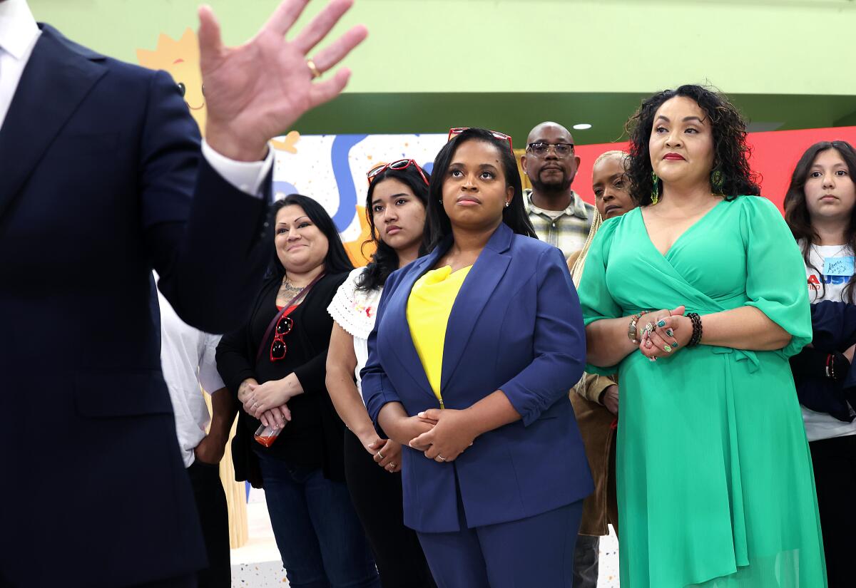 A woman in a blue suit stands with others at a press conference.  
