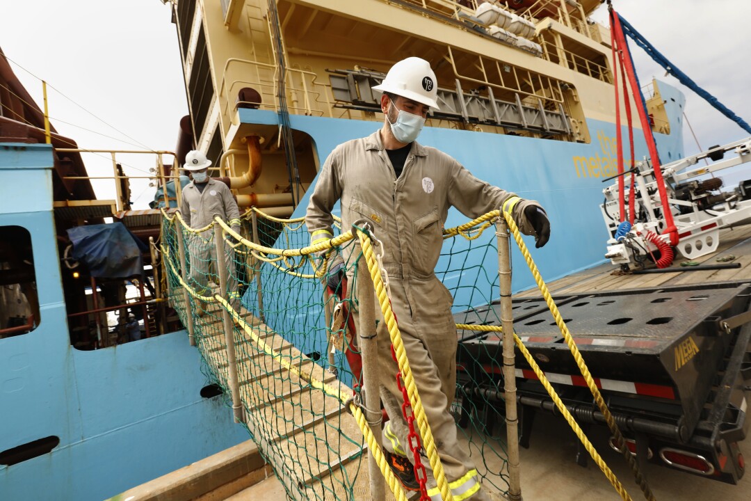 Workers disembark in San Diego from a large research vessel.