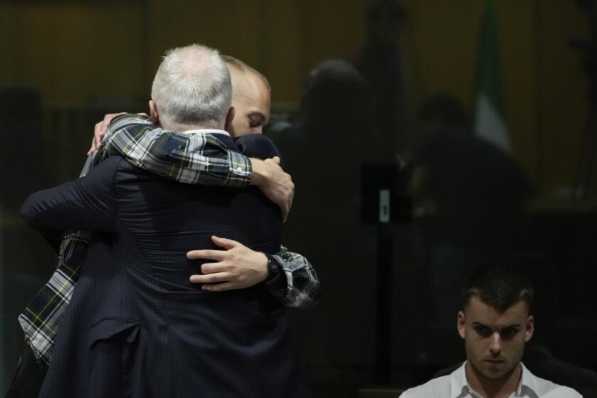 Ethan Elder, left, back to camera, father of Finnegan Lee Elder, hugs his son before the reading of the judgment at the end of a hearing for the appeals trial in which Finnegan is facing murder charges for killing Italian Carabinieri paramilitary police officer Mario Cerciello Rega, in Rome, Wednesday, July 3, 2024. At right sits Gabriel Natale Hjorth charged for the same killing. (AP Photo/ Alessandra Tarantino)