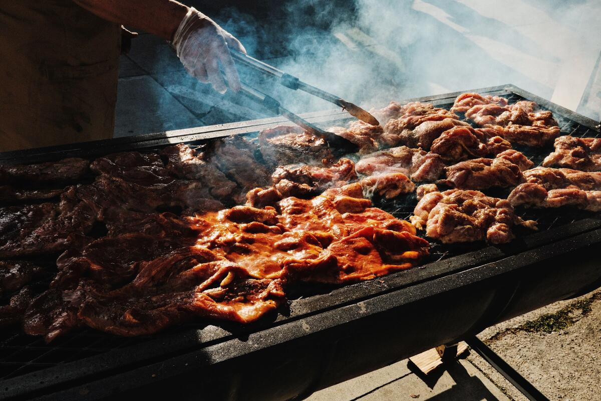 A hand holds tongs over a grill covered with meat.