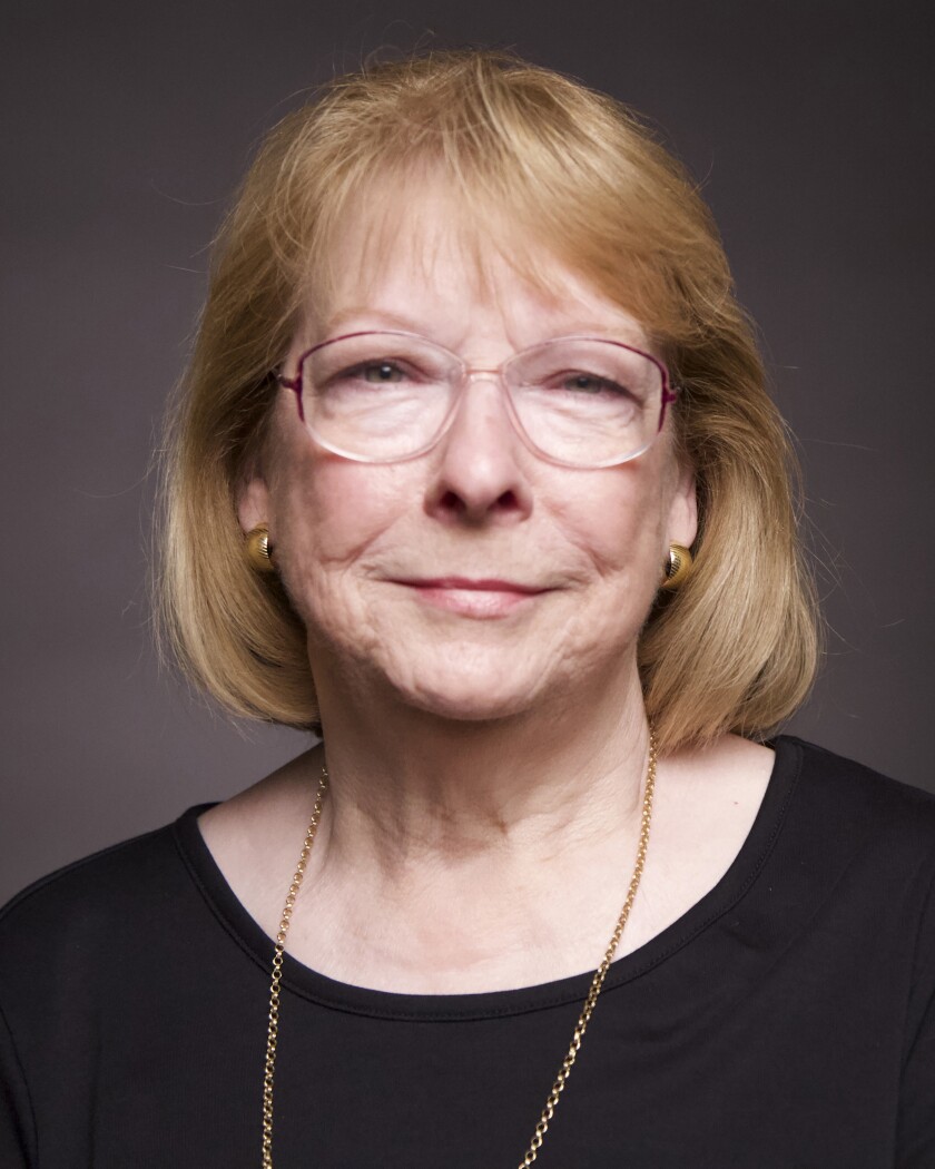 A portrait of a woman with glasses and shoulder length hair wearing a black shirt
