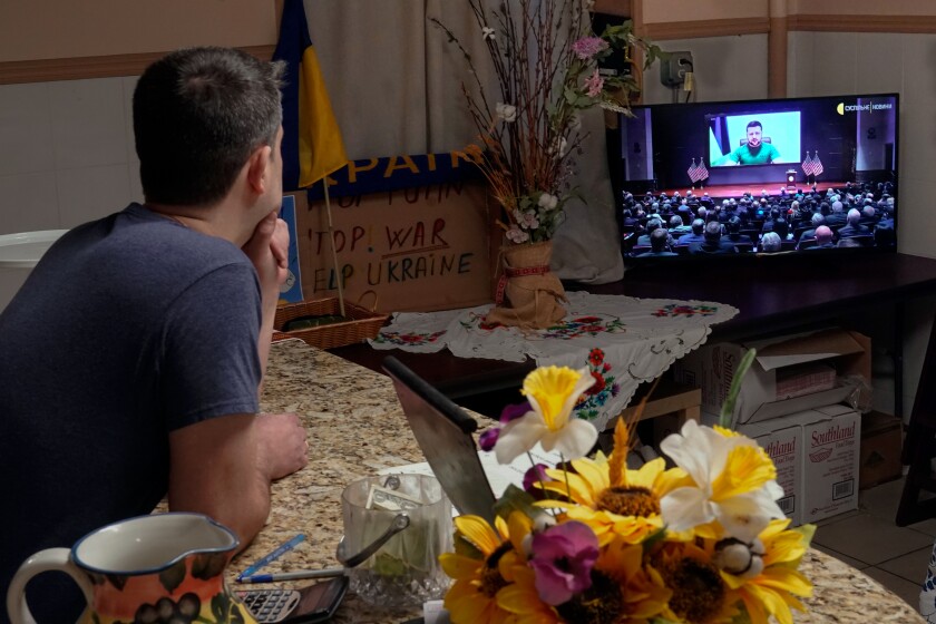 A man behind a counter watches Ukrainian President Volodymyr Zelensky on TV.