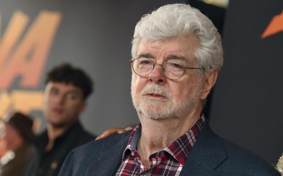 George Lucas in round glasses, a blue blazer and a plaid collared shirt.