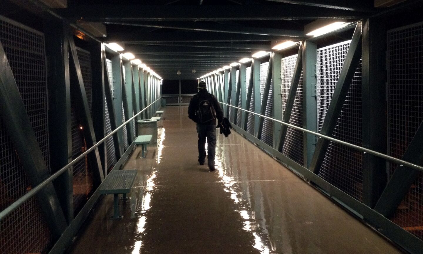 A commuter make his way across a pedestrian walkway at the Irvine Metrolink station as rain continues to fall in the Southland Friday morning.