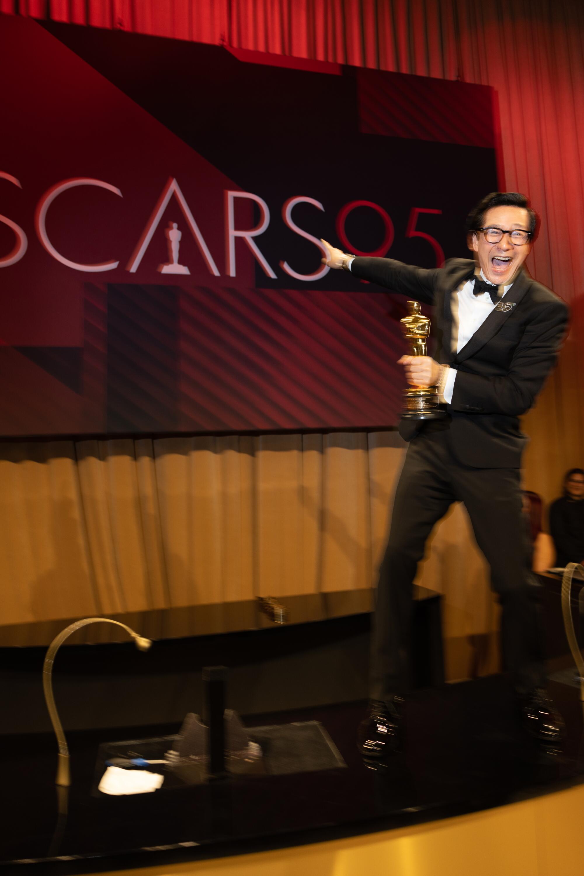 Ke Huy Quan, holding an Oscar, points at a sign reading, "Oscars."
