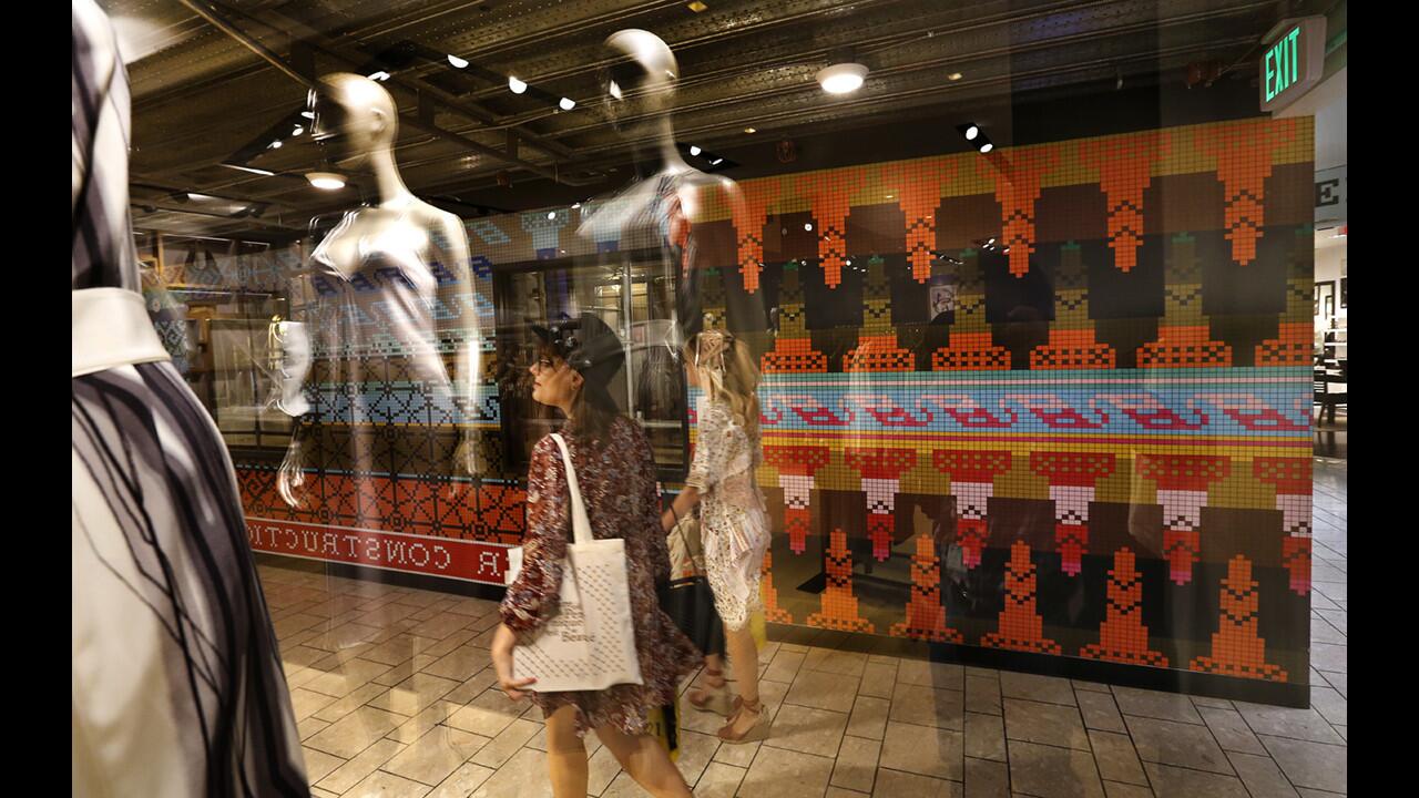 Shoppers walk past a construction barricade, background, decorated with artwork by Lisa Anne Auerbach titled "Strik Strikke, 2017," on the sixth floor of the Beverly Center in Los Angeles on April 20, 2017. The artwork, a vibrant wallpaper, is composed of hundreds of sweater patterns. Auergach's work is part of a Beverly Center art project that's morphing along with the building's $500-million renovation.