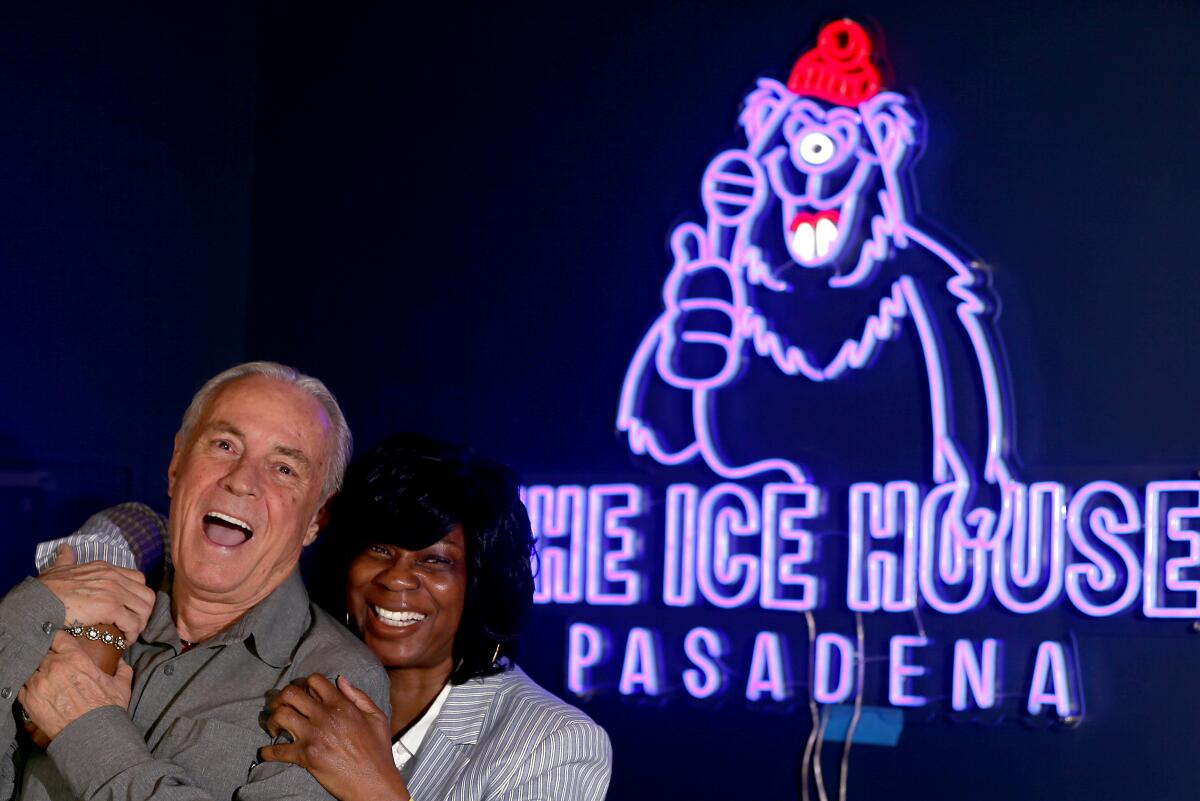 A man and a woman smile while standing next to a neon sign saying The Ice House Pasadena