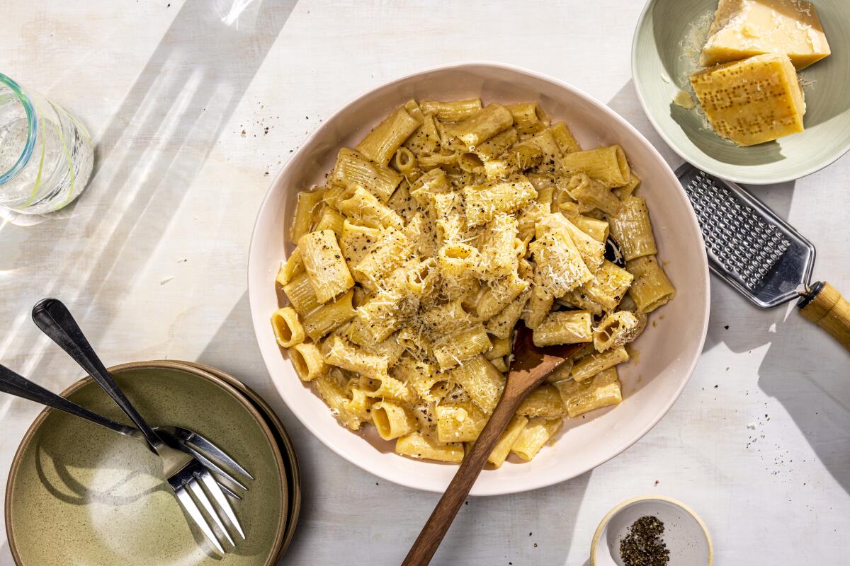 Rigatoni noodles with sprinkled Parmesan in a white bowl with a wooden spoon.