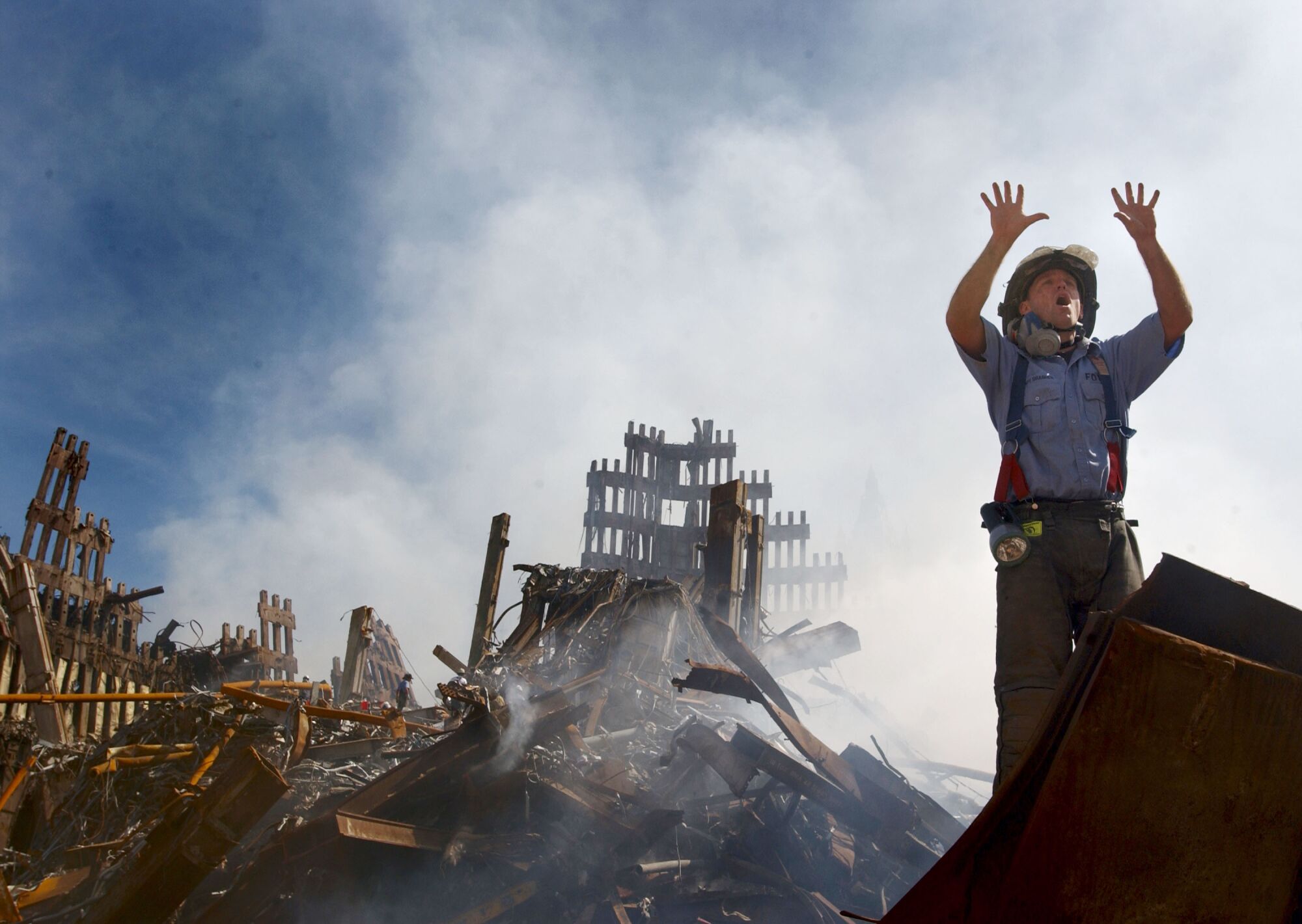 A firefighter holds up 10 fingers, standing before smoldering debris