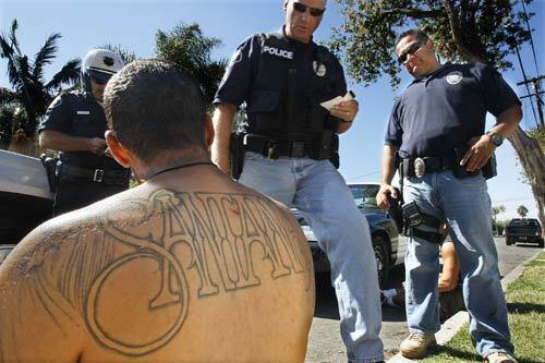 Santa Ana Police Sgt. Lorenzo Carrillo, right, listens as fellow officers talk with Armando Martinez on Aug 19, 2008. Martinez, heavily tattooed and known for his past gang affiliations, was stopped as he rode his bicycle on Franklin Street. He was released after questioning.