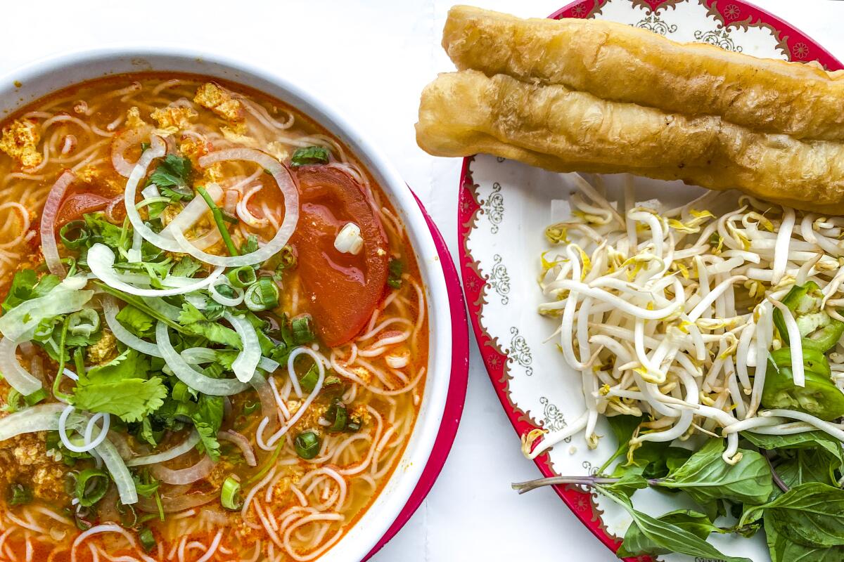 A bowl of noodle soup sits beside a plate of vegetable additions and you tiao.