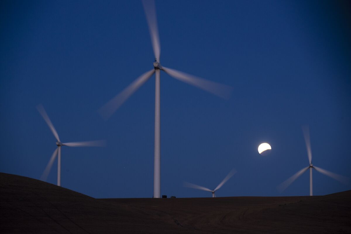 Turbines spin as the blood moon lunar eclipse sets behind the towers of the Shiloh II wind farm on May 26, 2021.