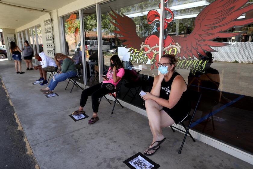 YUBA CITY, CA -- MAY 06: Customers wait in line on a first come first serve basis to have body piercings at Heart & Soul Tattoo on Wednesday, May 6, 2020, in Yuba City, CA. Every 30 minutes Wagner must stop and desensitize the table. The shop closes at 3 P.M. for an hour to sanitize the space. Sutter and Yuba counties, both north of Sacramento, are allowing businesses and restaurants to reopen, defying Gov. Gavin Newsom's statewide stay-at-home order due to the coronavirus pandemic. (Gary Coronado / Los Angeles Times)