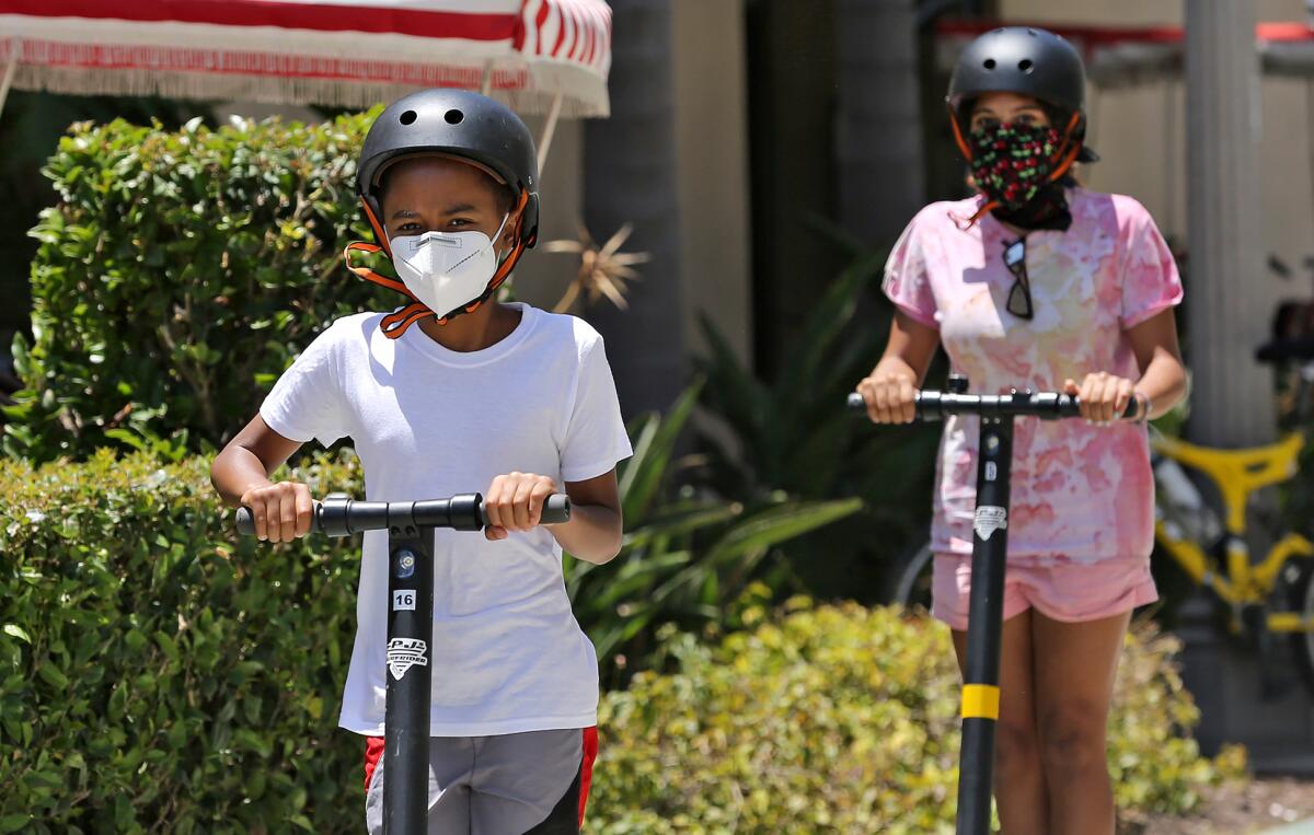 Youngsters on scooters roll down the bike trail near the Balboa Pier while wearing face coverings on Monday.
