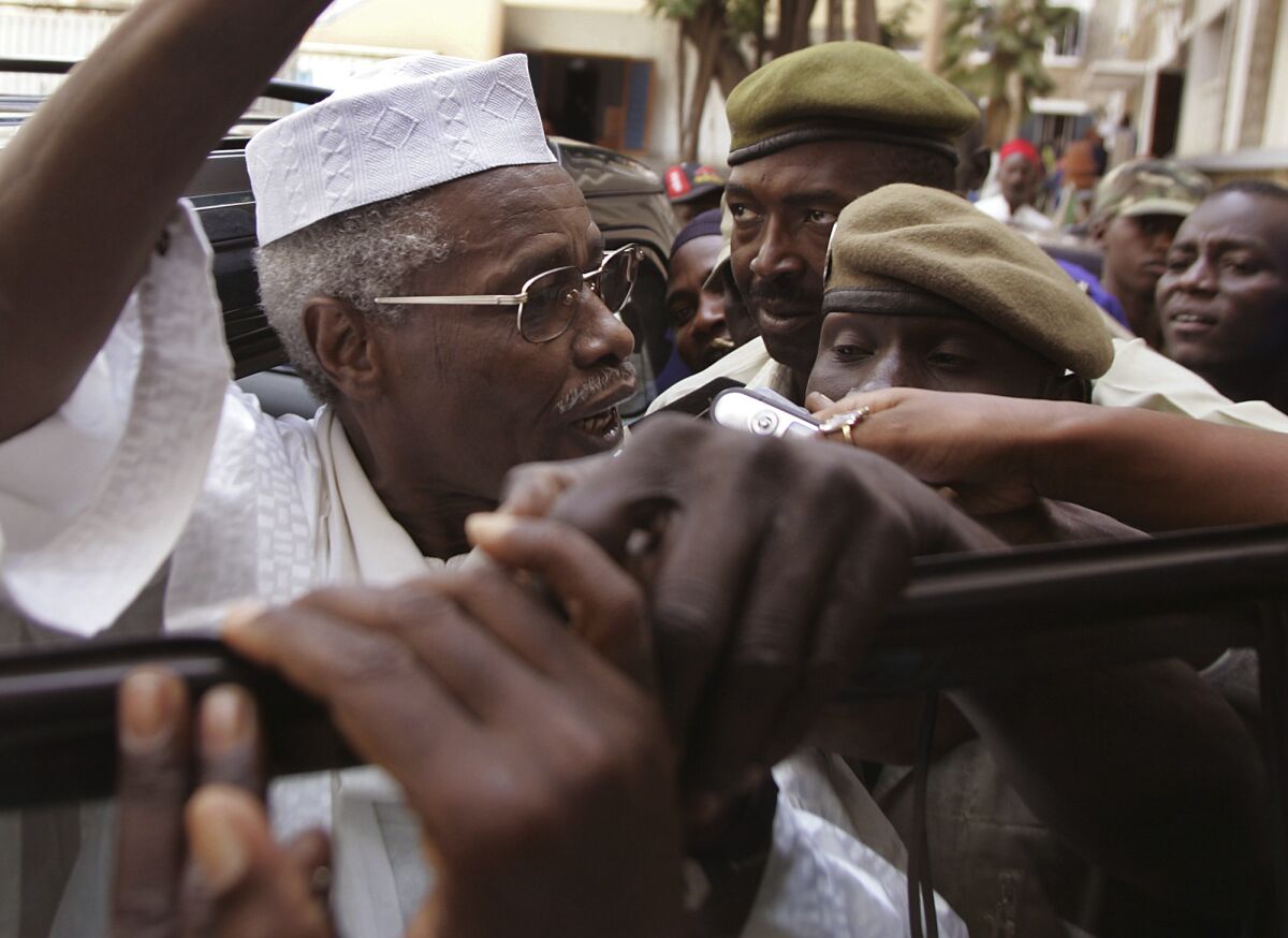 A man wearing glasses and a white hat is surrounded by people