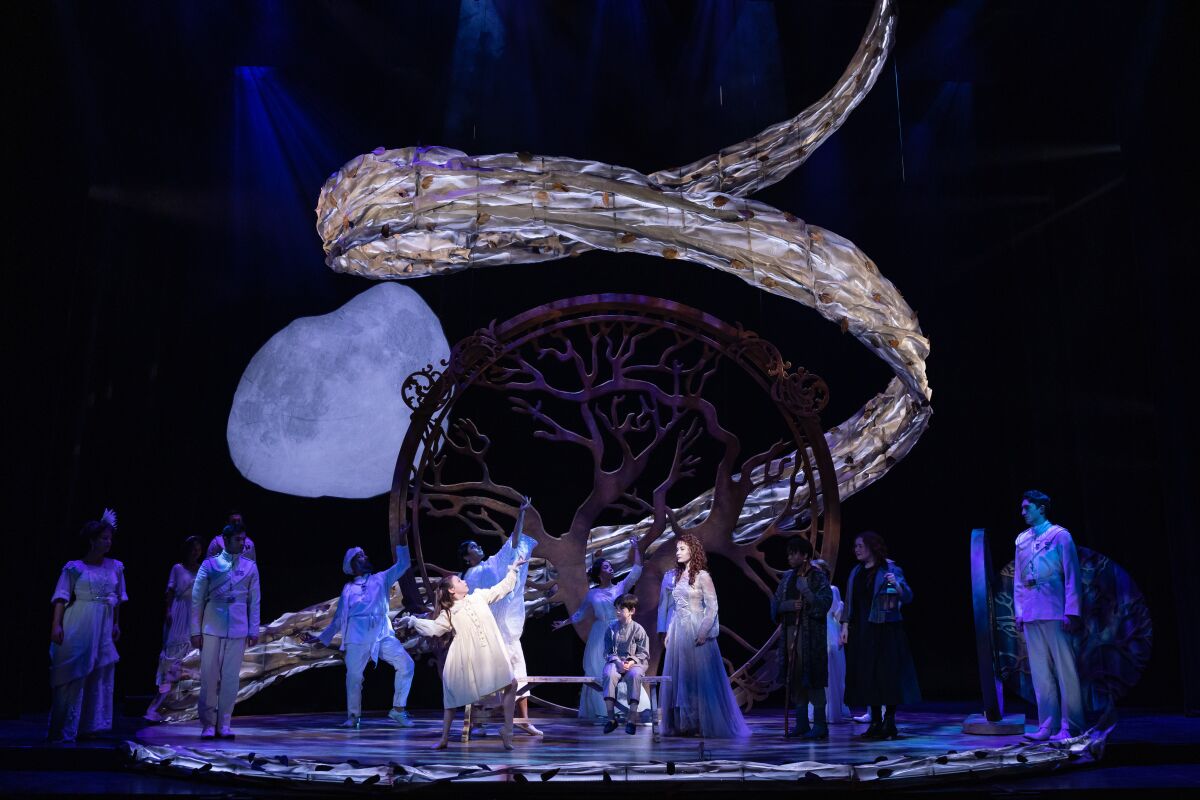 Actors perform in front of a stylized tree and glowing moon.