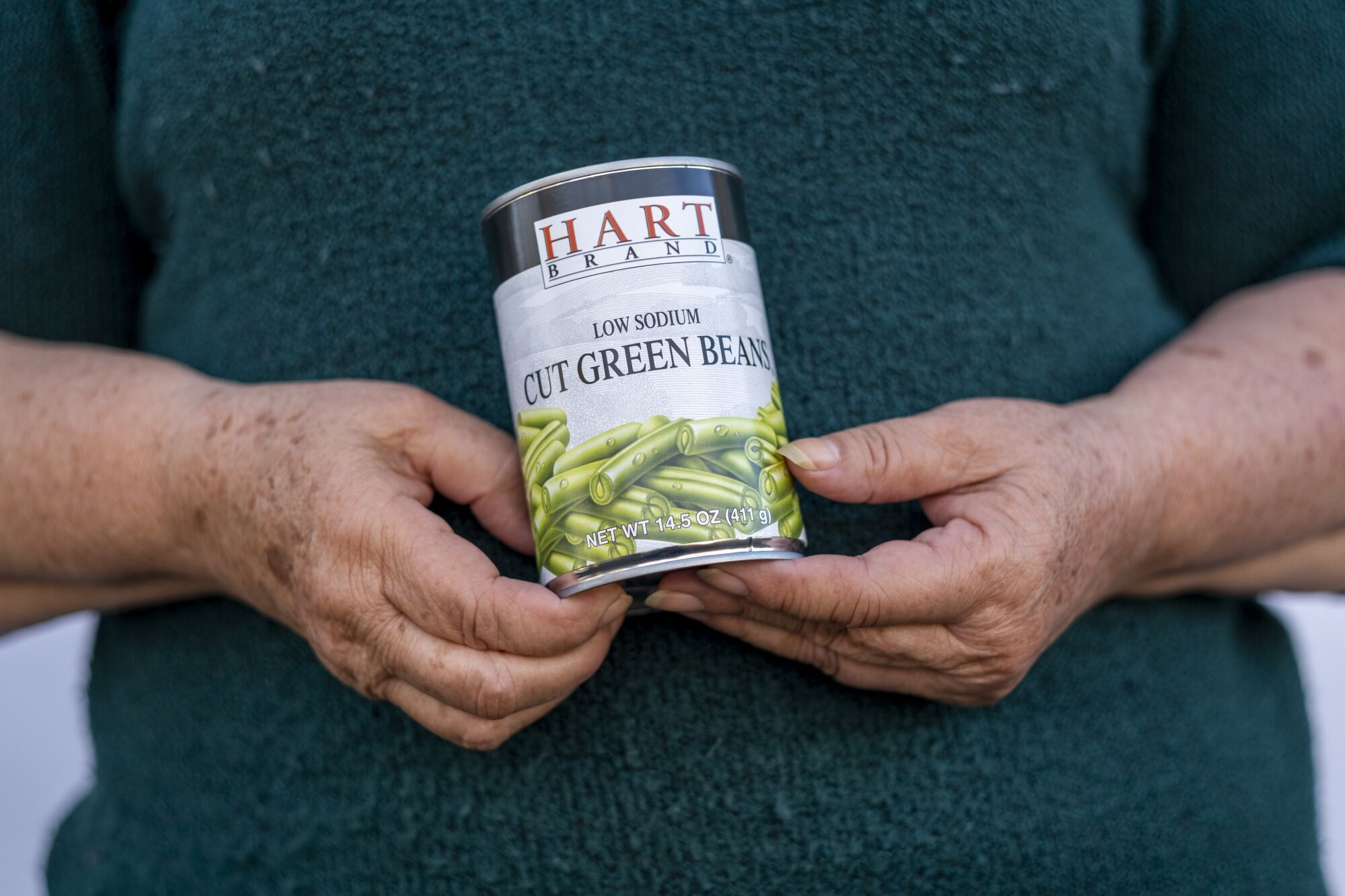 A woman holds a can of green beans. 