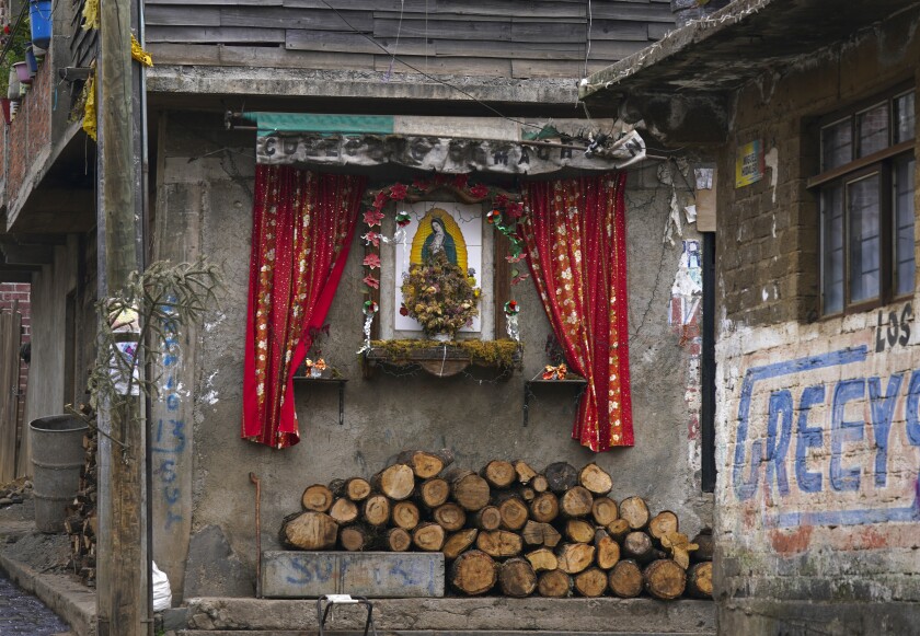 A Virgin of Guadalupe altar decorates the facade of a home where firewood used for cooking is piled below, in the Purepecha Indigenous community of Comachuen in Mexico's Michoacan state, Wednesday, Jan. 19, 2022. Money sent home by migrants working in the U.S. has allowed families to remain in Comachuen rather than moving to other parts of Mexico for work. (AP Photo/Fernando Llano)