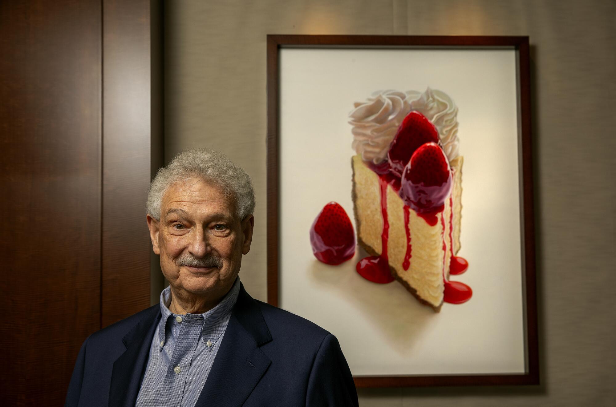 David Overton in front of a large painting of a cheesecake.