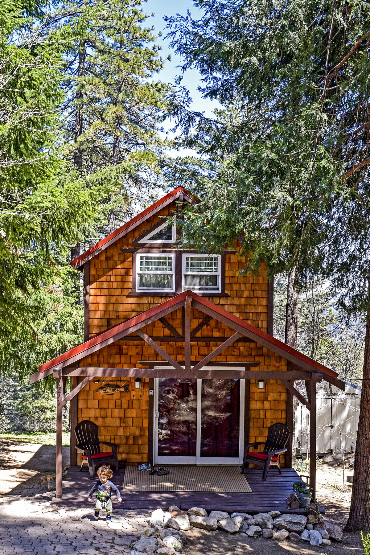 A small two-story wood house surrounded by conifers