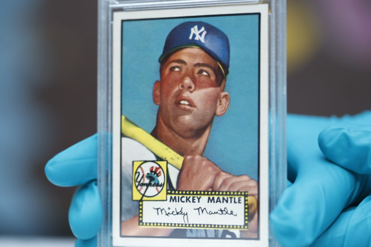 A closeup of hands in blue plastic gloves holding a plastic-encased baseball card with an image of Mickey Mantle.