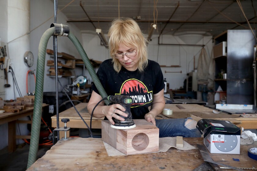 A woman in a woodworking studio uses a mechanical sander on a wooden box 