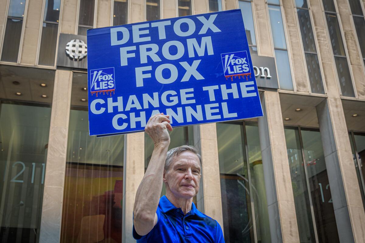 A protester with a sign that says "Detox from Fox. Change the channel"