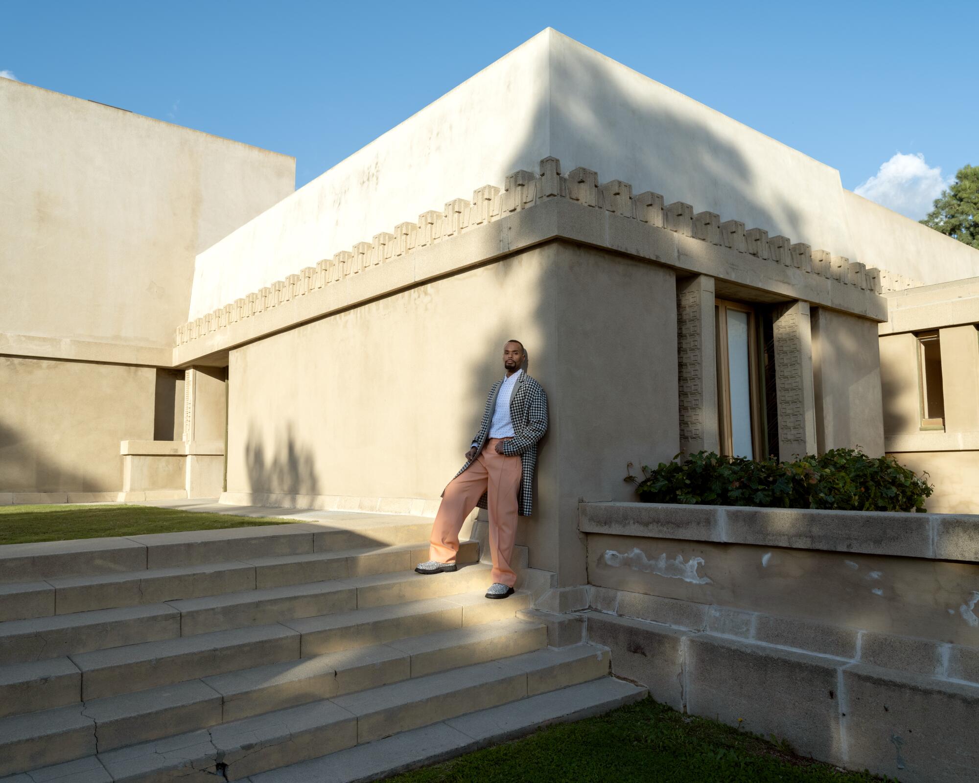 A man wearing orange trousers leans against the exterior of the Hollyhock House.