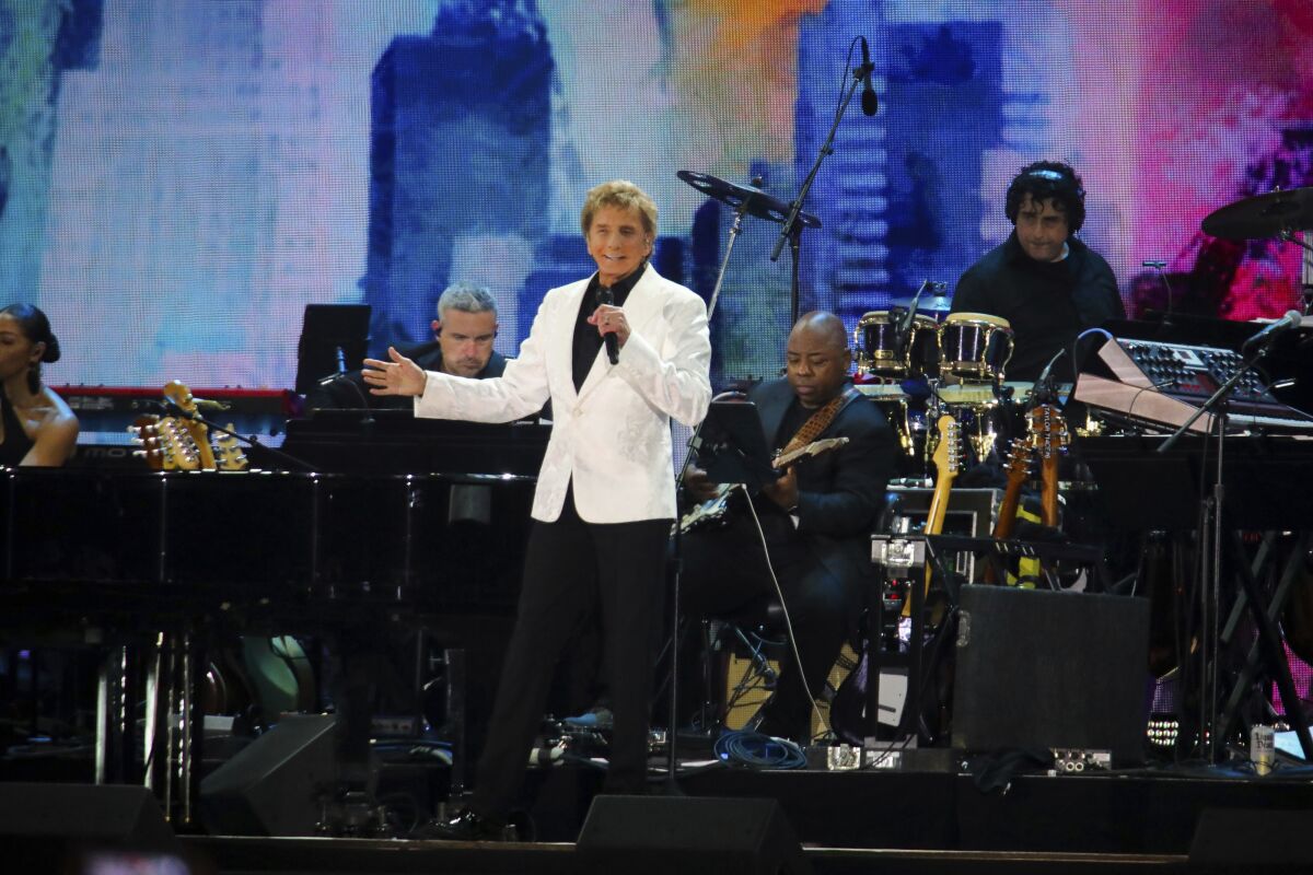 Barry Manilow performs onstage with musicians playing behind him
