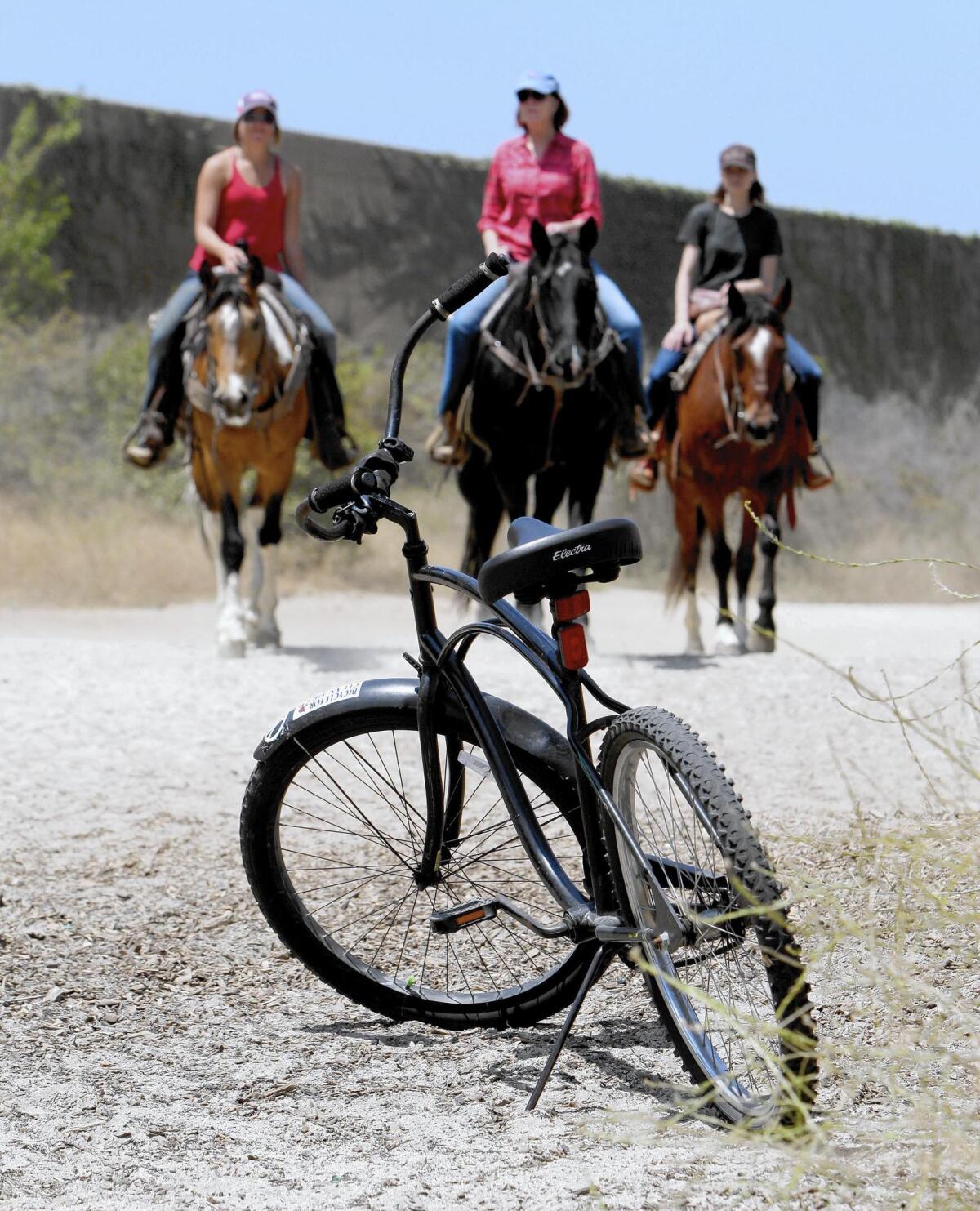 With a bicycle parked nearby, Rocken P Stables horseback riding guide Alyssa Conklin, left, leads two riders towards the Mariposa Street bridge in Burbank.