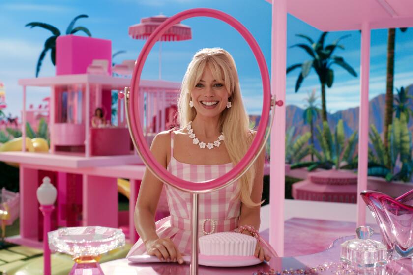 Margot Robbie as Barbie smiles in front of a mirror inside a pink doll house.