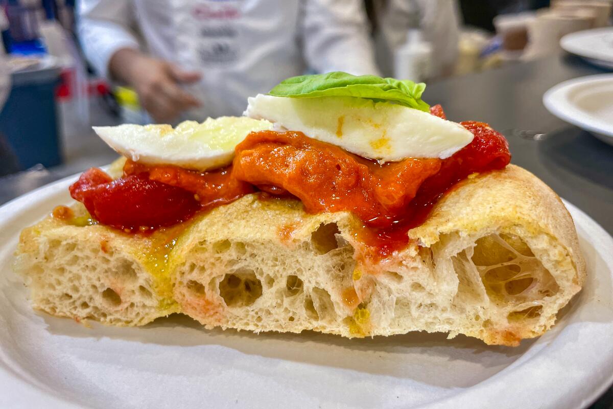 A slice of focaccia spianata topped with crushed tomato, mozarella di bufala and fresh basil