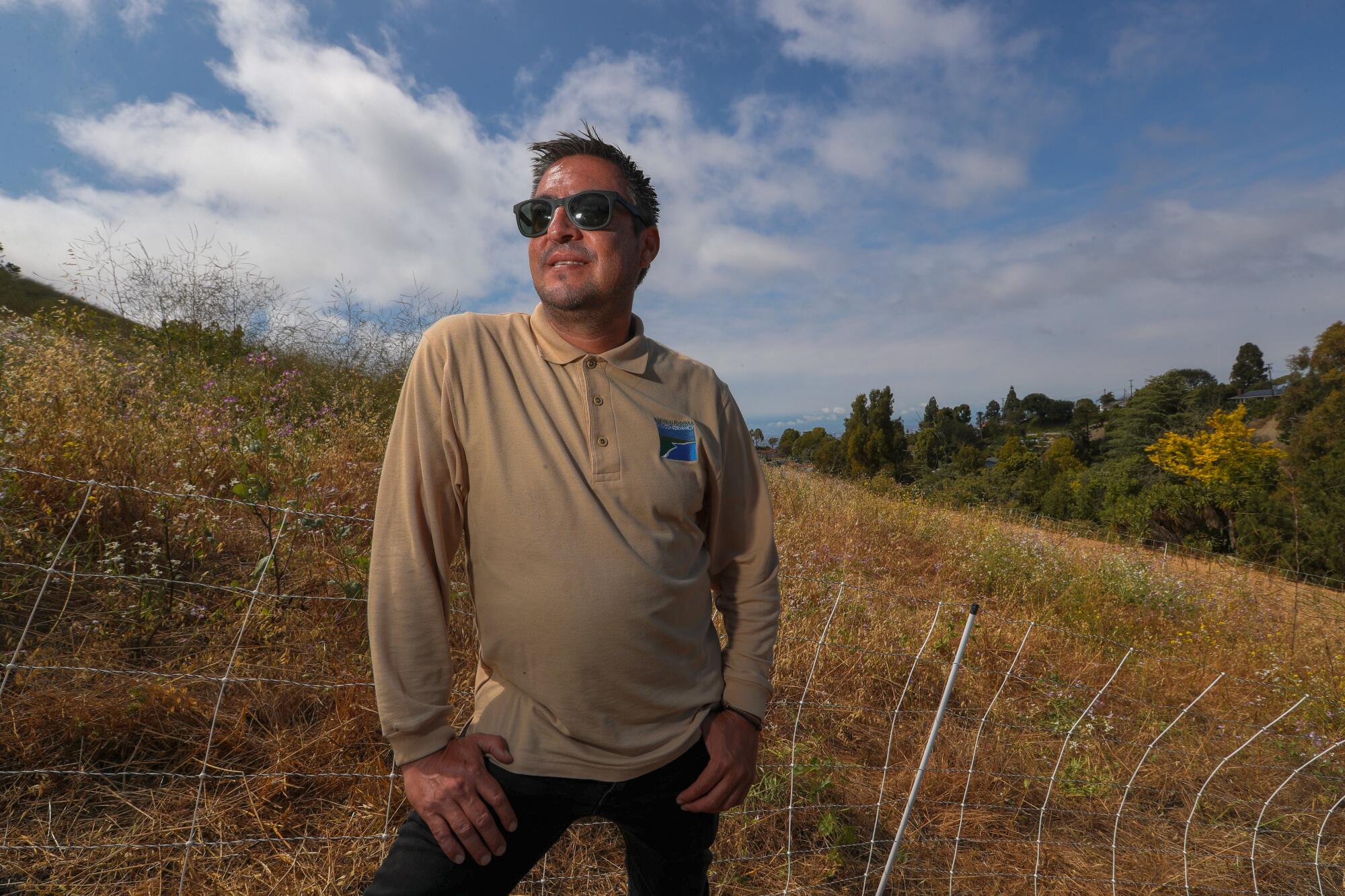 Cris Sarabia stands next to an electric fence on a hillside.