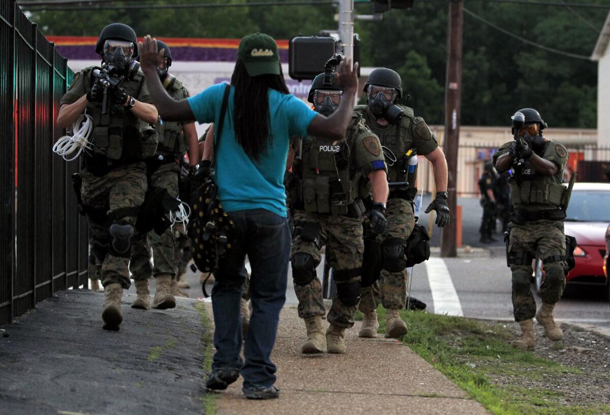 Police wearing riot gear walk toward a man with his hands raised on Aug. 11, 2014, in Ferguson, Mo.