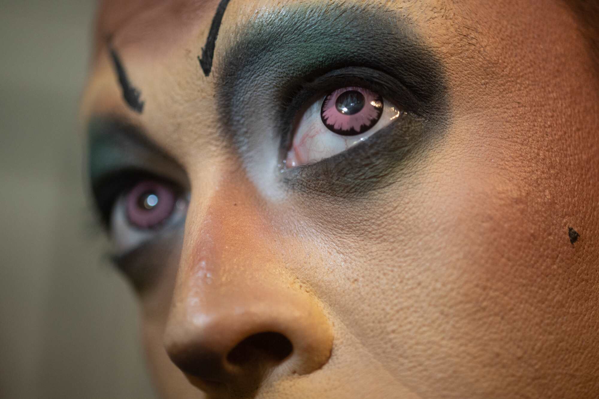 A close up of a man's face, wearing dramatic brown-colored contact lenses and makeup.