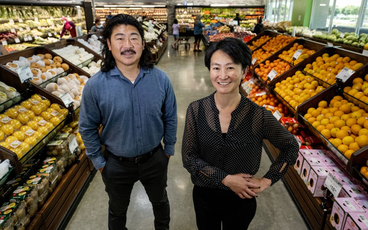 A man and a woman stand in a produce aisle at a grocery store
