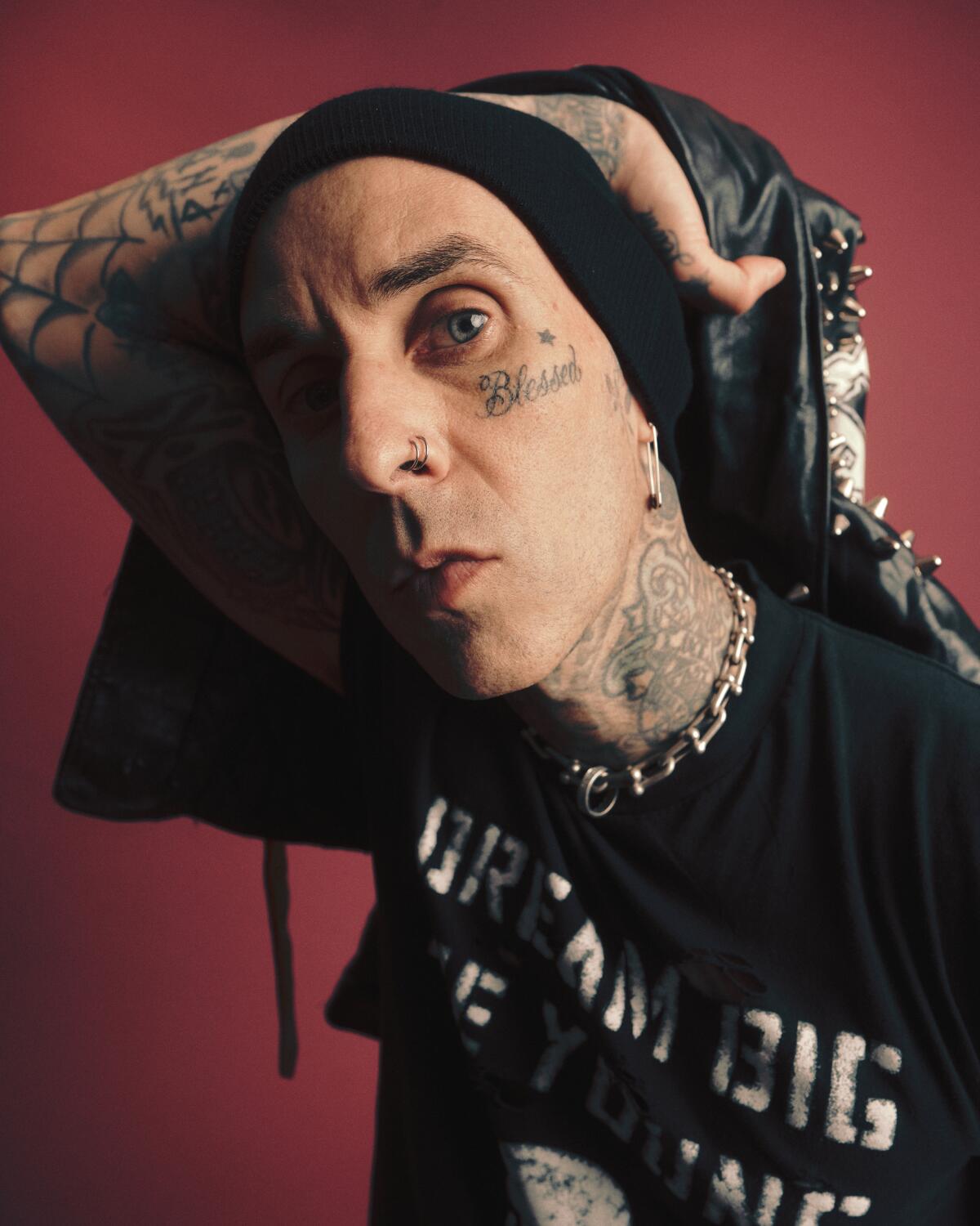 Travis Barker peers into the camera lens with his arm over his head and shadow on half his face