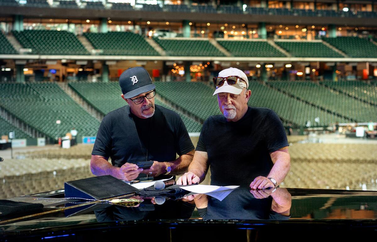 Billy Joel, right, with his creative director Steve Cohen, looks at notes while standing onstage in an empty arena.
